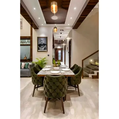 An elegant dining area designed for family gatherings. The space features comfortable upholstered chairs, a marble-top table, and a high ceiling with modern pendant lighting, creating a sense of grandeur.
