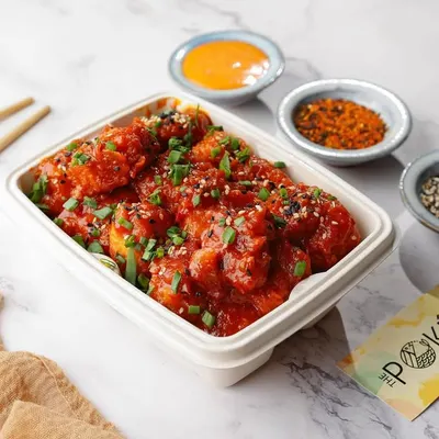 Saucy Korean fried chicken in a biodegradable takeaway container, styled with dipping sauces to look like a complete and tempting meal.