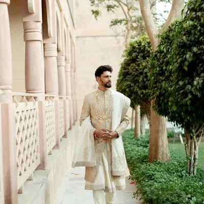 A classic portrait of the groom looking dapper in his wedding sherwani. Captured in a beautiful architectural setting, this photo exudes elegance and style.