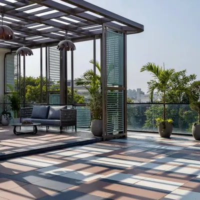 A perfect balance of shade and sun. This terrace in Faridabad features a slatted wooden pergola over a comfortable seating area, with large potted palms adding a touch of the tropics. The patterned floor tiles add a layer of visual interest to the design.