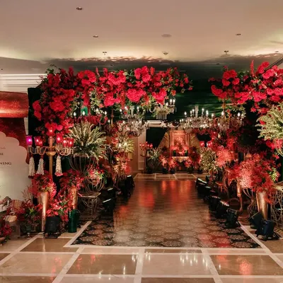 A grand entryway draped in a canopy of red blooms and illuminated by crystal chandeliers. This opulent passage sets a regal tone, welcoming guests into a celebration of timeless elegance.