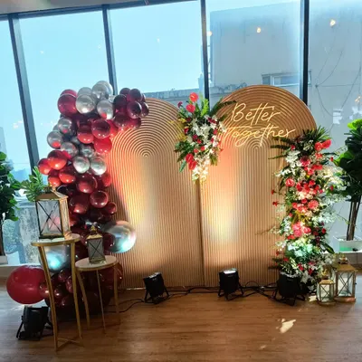 I created this 'Better Together' setup for a romantic celebration. It features twin ribbed wooden backdrops, beautiful red and white floral arrangements, and a balloon garland in shades of red and silver, all illuminated by a warm neon sign.