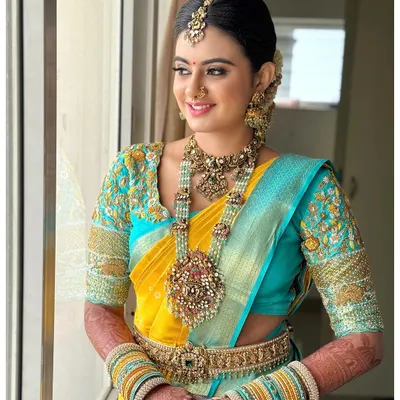 A full view of a bride looking radiant in our 92.5 silver-based bridal set with gold plating. The vibrant turquoise and yellow saree makes the intricate jewellery stand out beautifully.
