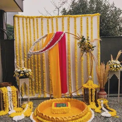 For this Haldi ceremony, I designed a setup that blends tradition with modern elegance. The backdrop features strings of vibrant marigolds, while the seating area is defined by a beautiful urli, all framed by a contemporary golden ring draped in rani pink and yellow fabric.