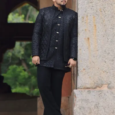 A model wearing a handcrafted black Indo-Western outfit. The layered look, with its textured jacket and tonal kurta, speaks power and elegance in every detail.
