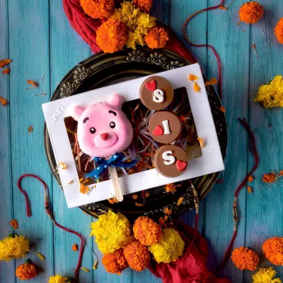 Rakhi is a special celebration of the bond between siblings. This adorable hamper for a sister includes a cute pink teddy bear cakesicle and Oreo-filled chocolates that spell out "SIS," all beautifully presented in a festive box.