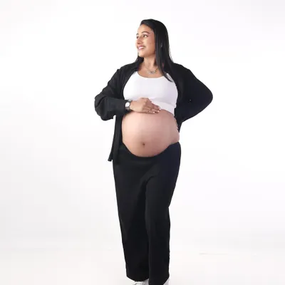A simple and happy portrait against a clean white background. Dressed in casual clothes, this mom-to-be shows off her beautiful baby bump with a confident smile.