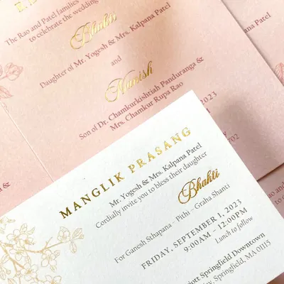 A close-up of a classic invitation with elegant gold foil lettering on soft pink and white cards. The delicate, line-drawn floral details add a touch of romance to the clean and timeless design.