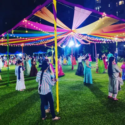 A wide shot of a Dandiya Night in full swing under the colorful canopy. This shows how the lighting and decor create a festive environment for guests to dance and celebrate Navratri.