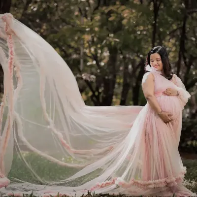 A breathtaking outdoor shot where the mom-to-be's pink gown and veil seem to float in the air. The natural park setting adds a touch of fairytale magic to this maternity portrait.