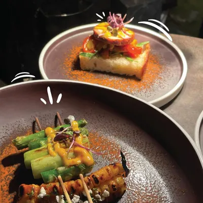 A display of our diverse international canapés. This pairing features grilled asparagus skewers with a creamy sauce and feta, alongside an open-faced toast topped with cured meat, showcasing our creative approach to global appetizers.