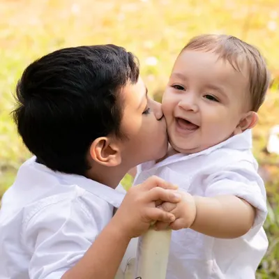 A beautiful family portrait outdoors, with a big brother giving his baby brother a sweet kiss on the cheek. These are the moments that matter.
