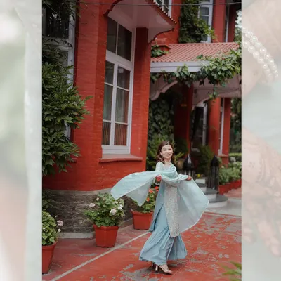 A candid shot of a woman in a beautiful blue sharara, twirling happily in the courtyard of a heritage hotel during her engagement celebration.