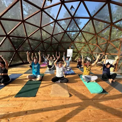 A group of students practicing a seated pose with arms raised, energizing the spine and opening the chest. This moment captures the collective energy and focus during one of our indoor yoga workshops.