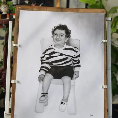 The completed portrait of a young boy on my drawing board, surrounded by the greenery of my studio.