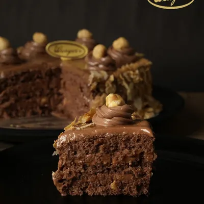 A perfect slice of our Nutella Hazelnut Cake. You can see the layers of moist chocolate sponge and rich Nutella cream, with a satisfying crunch from the nougat. It’s a slice of pure happiness.