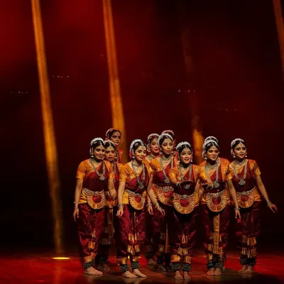 Our Bharathanatyam ensemble in a powerful opening formation, illuminated by dramatic stage lighting. Each performance is a culmination of months of dedicated practice and teamwork.