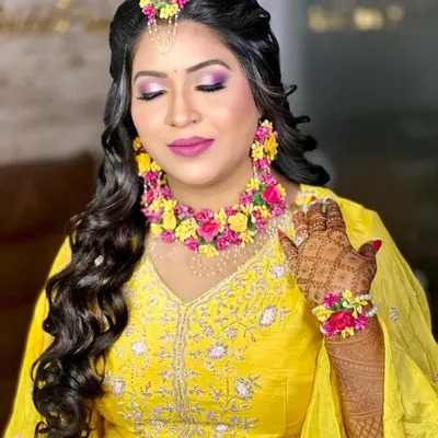 A beautiful bride ready for her Haldi ceremony. She is wearing a vibrant set of pink and yellow floral jewellery that perfectly complements her yellow outfit.