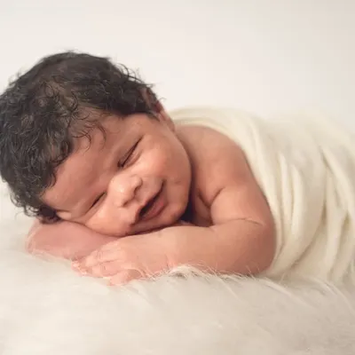 A perfect sleepy smile. I focus on capturing these fleeting moments against a simple, soft white background to keep all the attention on your baby's sweet expression.