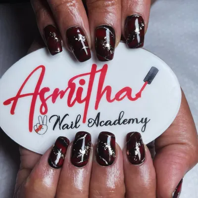 A detailed look at our red and black marble nail art, held against our Asmitha Nail Academy logo. The gold foil flakes add a touch of glamour to the design.