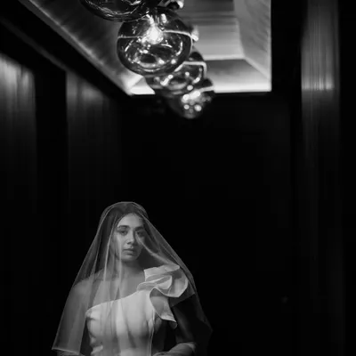 A bride veiled in shadow, illuminated by a row of vintage bulbs. This dramatic black and white portrait is a perfect example of how I use light and composition to create something truly artistic and memorable.