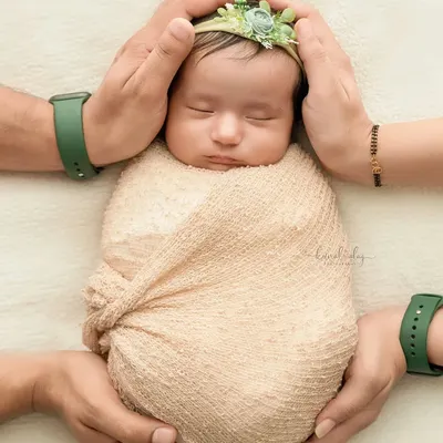 A newborn is held securely by their parents' hands, showcasing a classic and safe pose that emphasizes the baby's small size and the family's protection.