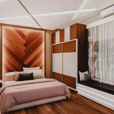 This bedroom design combines a warm, chevron-patterned wooden headboard with a practical two-tone sliding wardrobe and a cozy window seat, creating a perfect blend of style and comfort.