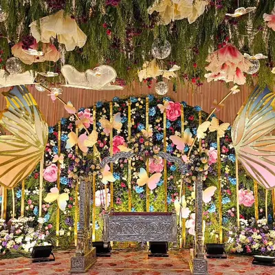 A full view of the enchanting butterfly-themed stage for a naming ceremony. The setup includes a silver cradle, a ceiling of hanging greenery and flowers, and large, shimmering butterfly wings.