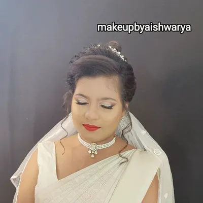 A beautiful Christian bride in a classic white saree and veil. The makeup is soft and luminous, with a bright red lip for a pop of color, and the hair is styled in an elegant updo.