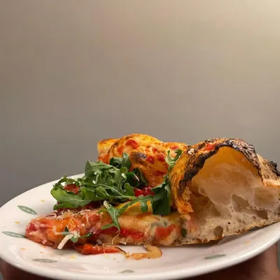 This is the result of all that dough science. A cross-section of a slice shows the open, airy crumb structure inside the cornicione. It's not doughy or heavy, it's light like a cloud.