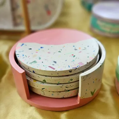 A set of four terrazzo coasters with a matching holder. This set features a half-pink, half-terrazzo design, making it a unique and functional piece of home decor.