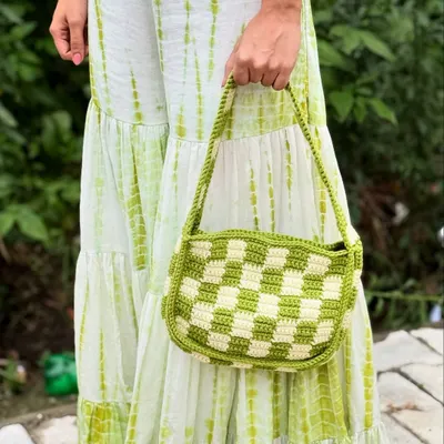 A full view of our handmade checkered crochet bag in a vibrant lime and white pattern, held against a matching tie-dye dress to show how it completes a look.