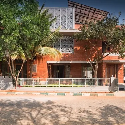 The Reshma Residence in Bangalore showcases a modern facade combining exposed brick with clean concrete lines and protective jaali screens. The design thoughtfully integrates mature trees on the plot, making the home feel connected to its environment.