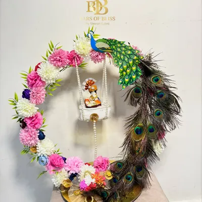 My most elaborate Janmashtami Jhula hamper. This design features a floral and peacock feather wreath around a swinging Ladoo Gopal, with a base of treats below.