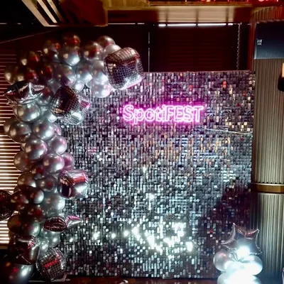 For the 'SpotiFEST' corporate event, we designed this high-impact photo wall featuring a shimmering silver sequin backdrop and a custom neon sign with the event's branding. This setup creates a modern, shareable experience for guests.