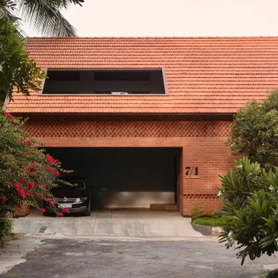 The entrance facade of the Ferns Cottage, featuring a distinctive Mangalore tile roof and detailed brickwork. The design provides a covered carport that is seamlessly integrated into the home's overall structure.