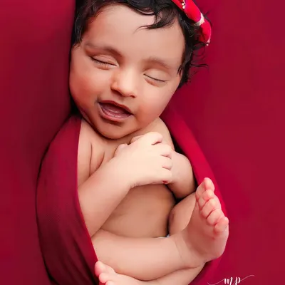 A dreamy smile from a newborn snugly wrapped in a rich red swaddle. We focus on capturing these fleeting expressions that reveal your baby's budding personality.