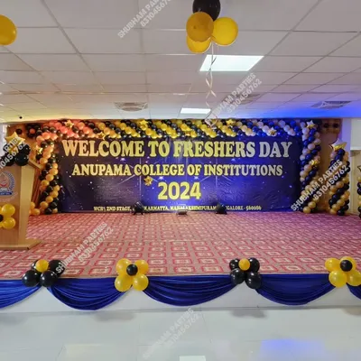 A grand stage decoration for a college Freshers Day, with a large banner and a black and yellow balloon arch.