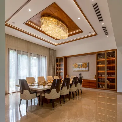 This luxurious dining room features a ten-seater marble table, a stunning crystal chandelier, and a custom-built wooden crockery unit, creating an elegant space for formal gatherings.