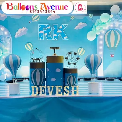 A charming hot air balloon theme for Devesh's birthday. The stage is decorated with a sky-blue backdrop, fluffy cloud cutouts, and a striped floor to complete the look.