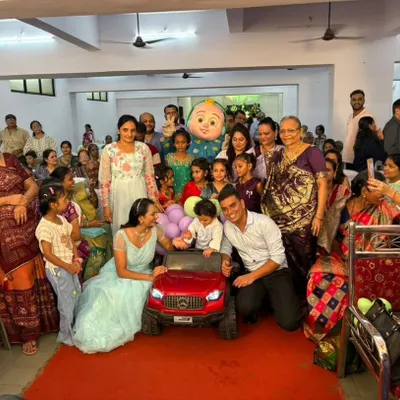 A wonderful group photo capturing the joy of a mascot appearance. The popular Cocomelon character stands among the children and family, posing for a picture after the birthday boy's grand car entry.