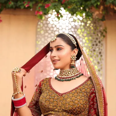 Achieve a royal bridal look with our curated kundan sets. This bride is wearing a beautiful choker with green bead detailing, a matching sheeshpatti, and a delicate hathphool for a complete, regal appearance.
