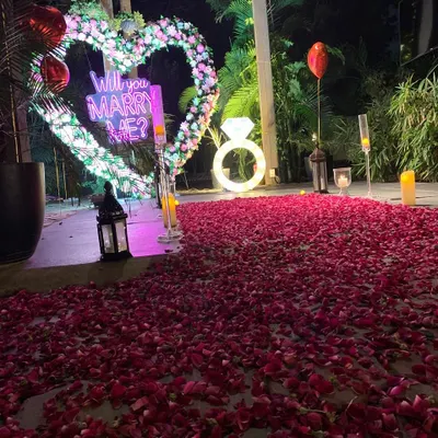 A close-up view of our popular outdoor proposal decoration. The glowing "Will You Marry Me?" sign and illuminated ring prop are perfectly framed by a floral heart, creating a picture-perfect setting.
