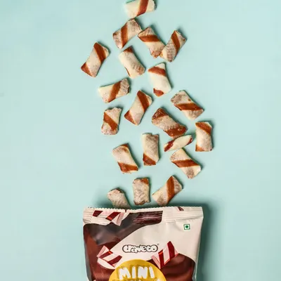 Mini vanilla bites appearing to fall out of the packet against a bright blue background. This dynamic "levitation" style of food photography is playful and captures a sense of fun.