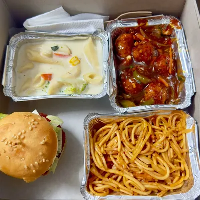 A look inside one of my popular multi-cuisine snack boxes. This one features a veg burger, white sauce pasta with broccoli, spicy veg manchurian, and hakka noodles, perfect for someone who loves variety.