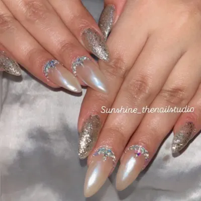 Shine bright with this combination of gold glitter and pearl chrome nails. This stiletto set is accented with a half-moon of rhinestones for extra sparkle.