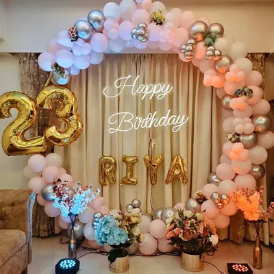 A beautiful circular balloon arch in pastel pink, peach, and silver for a 23rd birthday. The setup includes foil number balloons for the age and the birthday girl's name "RIYA" for a personalized touch.