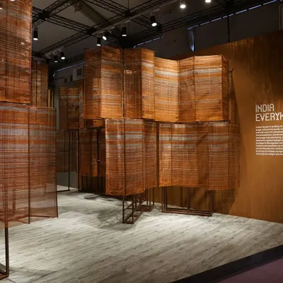 A wide view of the 'India Everywhere' installation, where handwoven metallic surfaces flow like a gleaming river. The structure, meticulously crafted with copper wires and cotton accents, transforms industrial frameworks into a singular, expressive sculptural form that speaks of tradition and modernity.