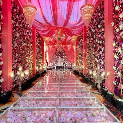Walking on a path of flowers. This stunning glass aisle filled with pink hydrangeas, surrounded by floral walls and elegant chandeliers, creates a true fairytale entrance for the bride and groom.