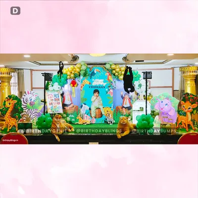 A wide view of our grand jungle-themed birthday stage, complete with a personalized backdrop, numerous animal props like a tiger and giraffe, and an expansive balloon arch in green and gold.